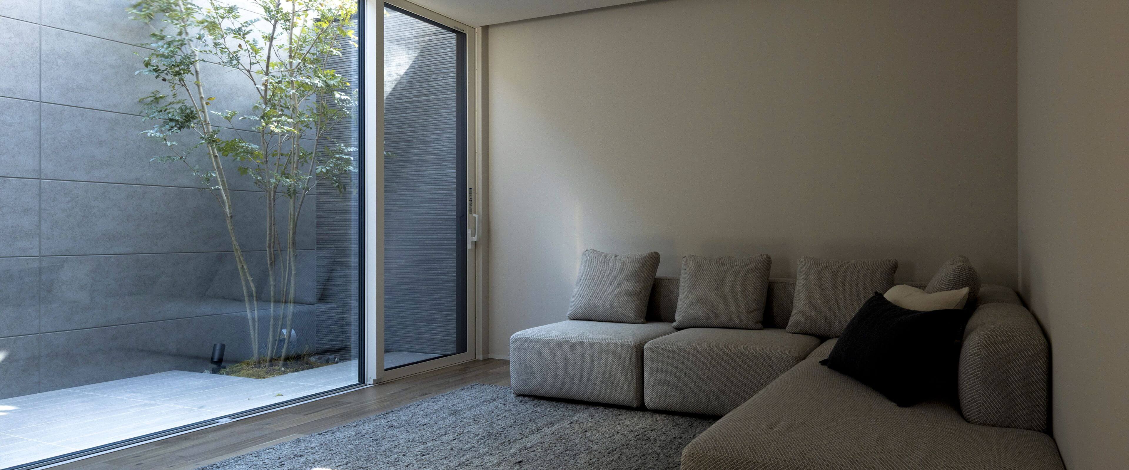 中庭に面した大開口の窓から光が差し込む、グレーのソファを置いた静かなリビングの様子