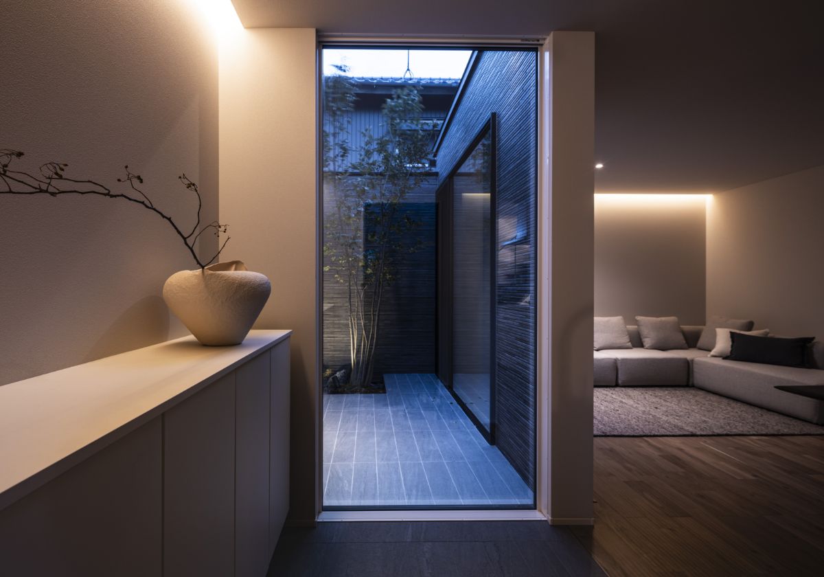 室内から中庭を望む細長い通路の先に、落ち着いた照明で整えられたリビングが広がる夜の様子