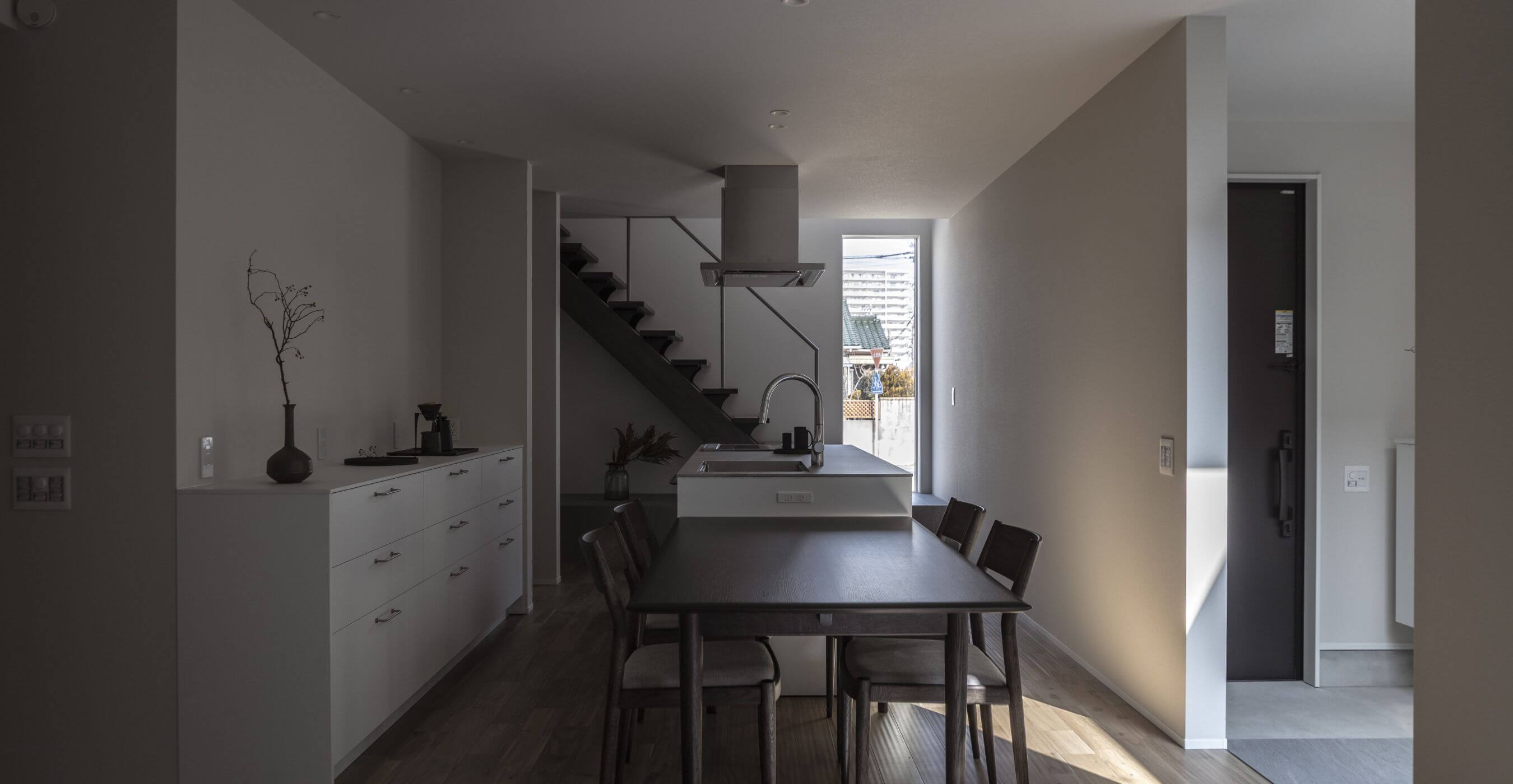 ダイニングと一体のアイランドキッチン奥に階段が見える、落ち着いたトーンのLDKの様子