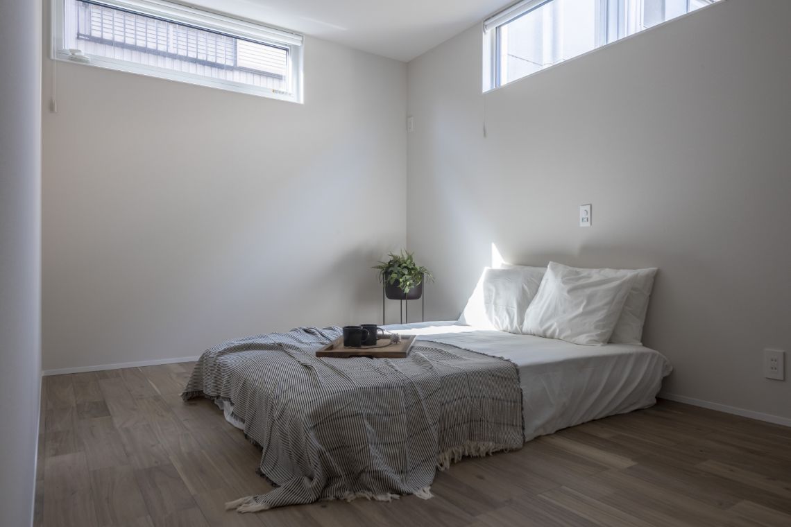 低めのベッドを置いた寝室に高窓からやわらかな光が入り、白い壁に包まれた静かな空間の様子